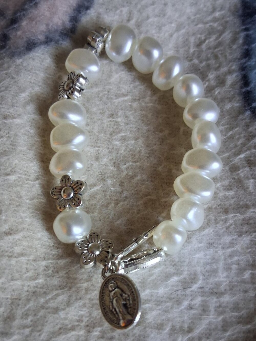 womans  pearl braclet with a cross and holy mother metel attached to it